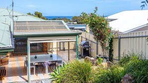 A covered outdoor patio with a table and chairs, a barbecue grill, and a view of the ocean. - Dive into Dorset - 10 Dorset Court (CARRICKALINGA)