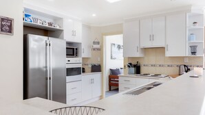 A modern kitchen with white cabinets, a built-in oven, a microwave, and a large island with a sink. - Dive into Dorset - 10 Dorset Court (CARRICKALINGA)