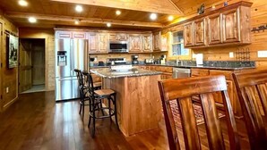 A spacious kitchen with wooden cabinets, a central island, and bar stools. - Sunset Ridge Lodge - Sunset Ridge Lodge - Breathtaking mountain views and (Bryson City)