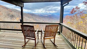 A wooden deck with two wooden chairs facing a scenic view of mountains and autumn foliage. - Sunset Ridge Lodge - Sunset Ridge Lodge - Breathtaking mountain views and (Bryson City)