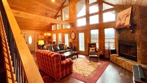 A spacious living room with a fireplace, wooden ceiling, large windows, and a staircase. - Sunset Ridge Lodge - Sunset Ridge Lodge - Breathtaking mountain views and (Bryson City)