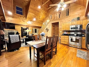 A wooden cabin interior with a dining area, kitchen, and a staircase leading to an upper level. - Tree Top Getaway close to Fontana Lake and NOC - Free Train Tix! (Almond)