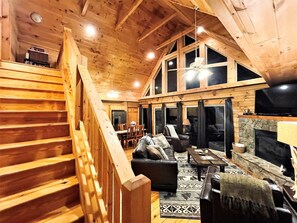 A wooden interior with a fireplace, a sofa, a dining area, and a staircase. - Tree Top Getaway close to Fontana Lake and NOC - Free Train Tix! (Almond)