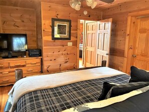 A wooden cabin room with a bed, a television, and a door leading to another room. - Tree Top Getaway close to Fontana Lake and NOC - Free Train Tix! (Almond)