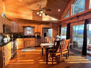 A wooden cabin interior with a kitchen, dining area, and large windows. - Tree Top Getaway close to Fontana Lake and NOC - Free Train Tix! (Almond)