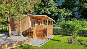 Eine Holzhütte mit überdachter Veranda, einer Sitzgelegenheit mit Bank und einem kleinen Garten mit Hecke und Baum.