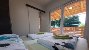 Ein Zimmer mit zwei Betten, jeweils mit gemusterten Bettdecken und Kissen, einer Holzbalkendecke und einem großen Fenster mit Blick auf Grünflächen.