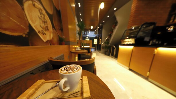 A coffee cup with latte art on a wooden tray at a cafe with wooden furniture and a modern interior. - Ruby Royal Hotel (Istanbul)