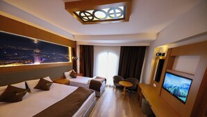 A hotel room with two beds, a TV, a desk, and a view of a cityscape at night. - Ruby Royal Hotel (Istanbul)