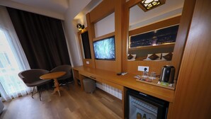 A hotel room with a wooden desk, a television, a mini-fridge, and a seating area with a chair and table. - Ruby Royal Hotel (Istanbul)