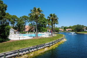 Une propriété située au bord de l’eau, dotée d’une piscine, de chaises longues, de palmiers et d’une fontaine.
