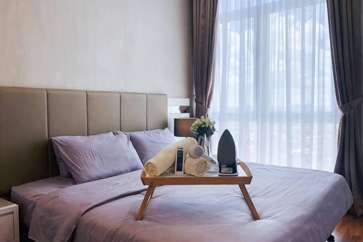 A hotel room with a bed, a bedside table, a tray with towels, and a window with curtains.