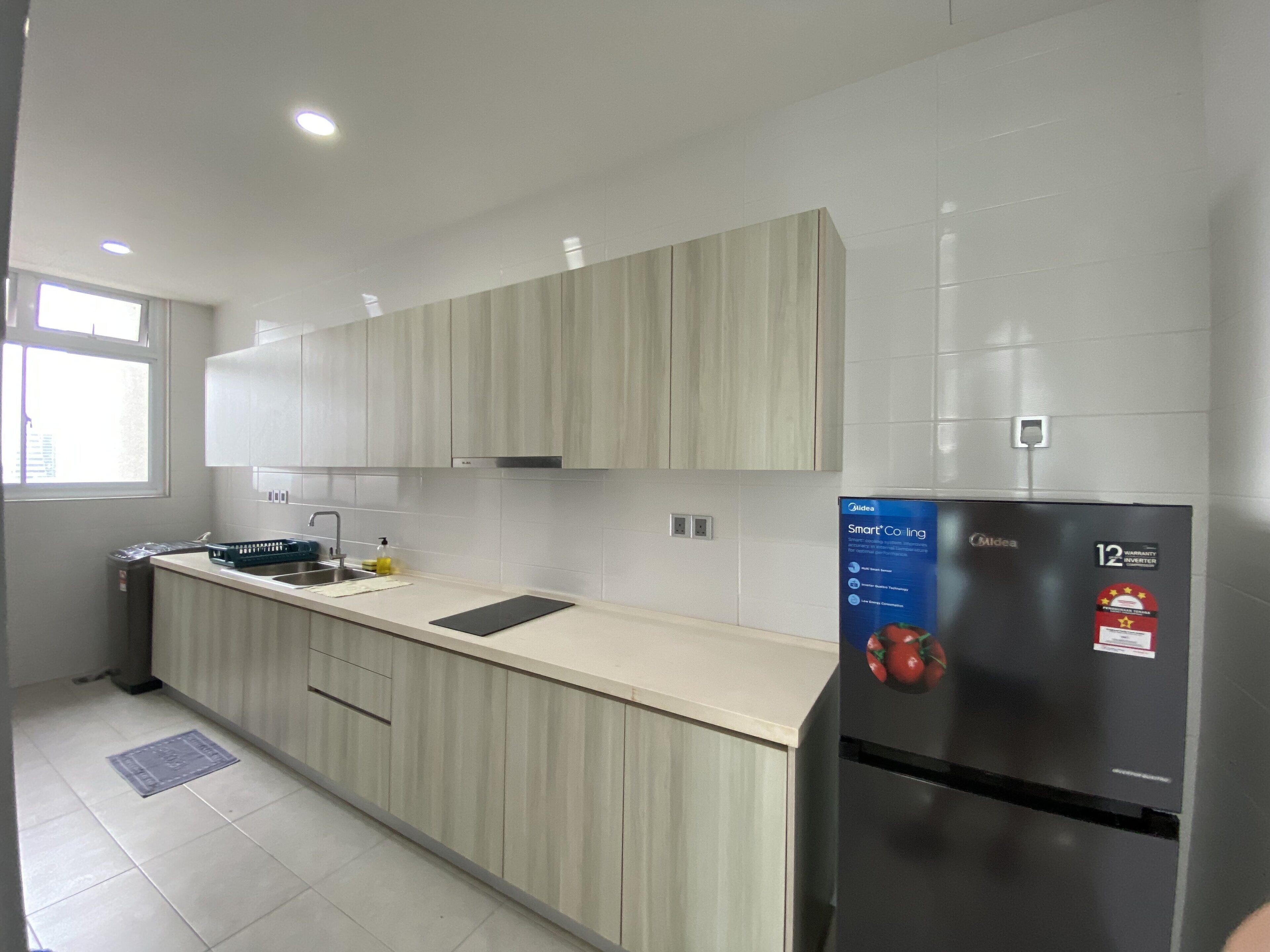 A modern kitchen with light wood cabinets, a stainless steel refrigerator, and a built-in oven.
