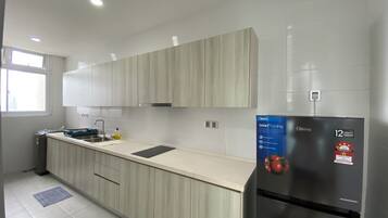 A modern kitchen with light wood cabinets, a stainless steel refrigerator, and a built-in oven.