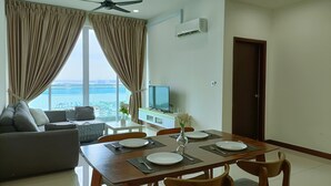 A modern living room with a dining area, large windows with curtains, a ceiling fan, and an air conditioning unit. - Paragon Suite By Antlerzone (Johor Bahru)