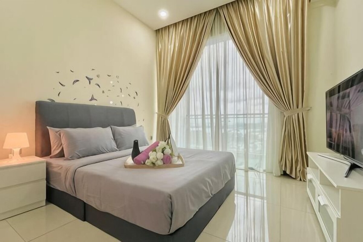 A bedroom with a bed, bedside table, TV, and curtains.