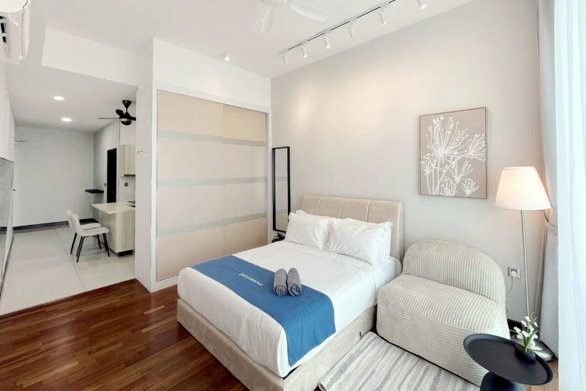 A modern hotel room with a bed, bedside table, chair, and a desk with a chair.