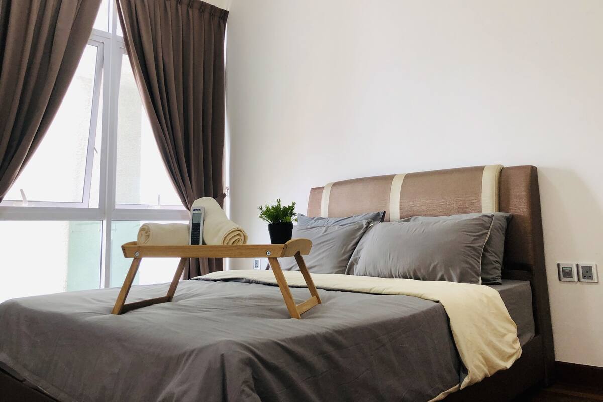 A neatly made bed with a wooden headboard, a bedside table with a lamp, and a window with curtains.