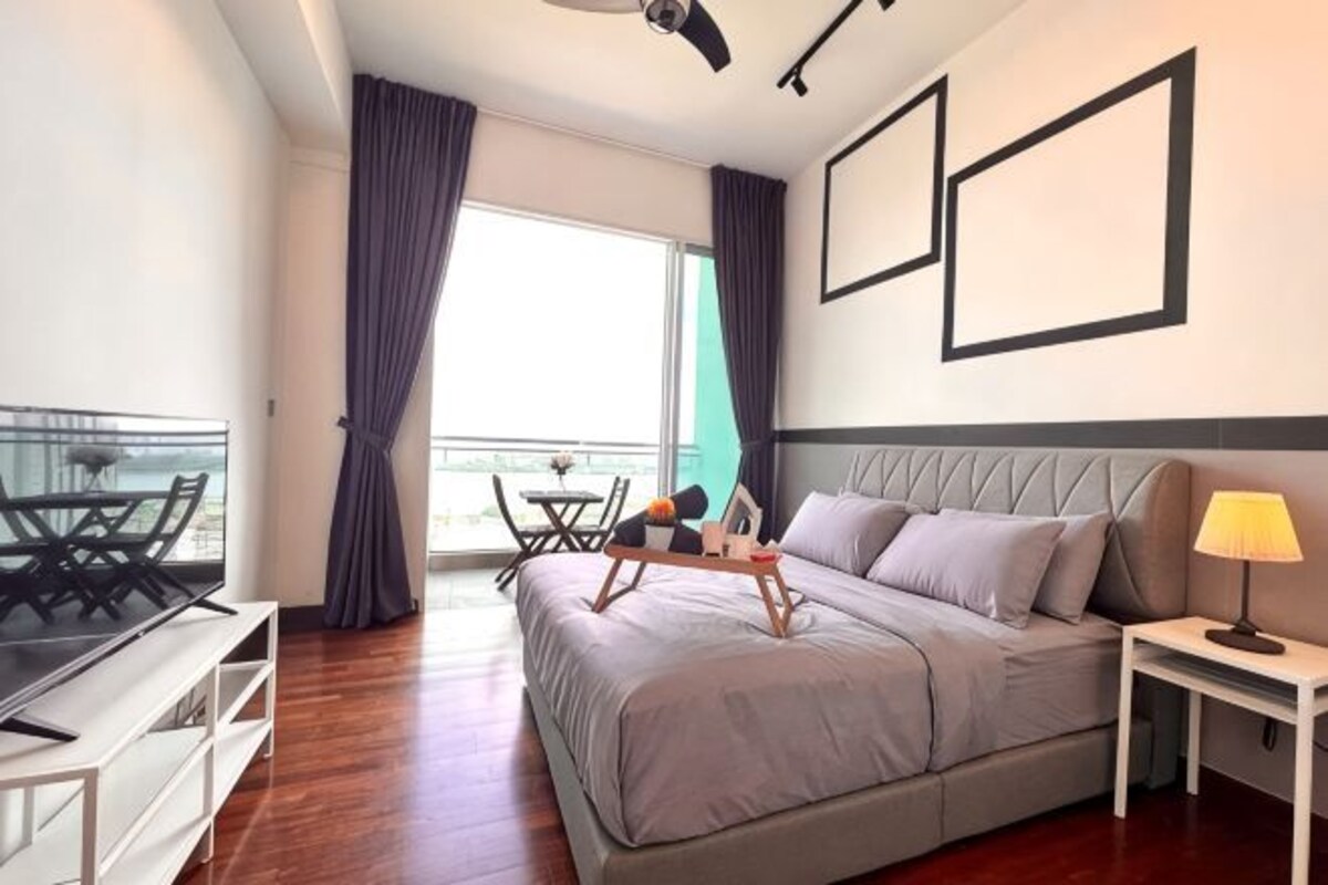 A modern hotel room with a bed, bedside table, lamp, and a balcony with a table and chairs.