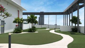 A modern building with a rooftop garden featuring artificial grass, palm trees, and a pathway.