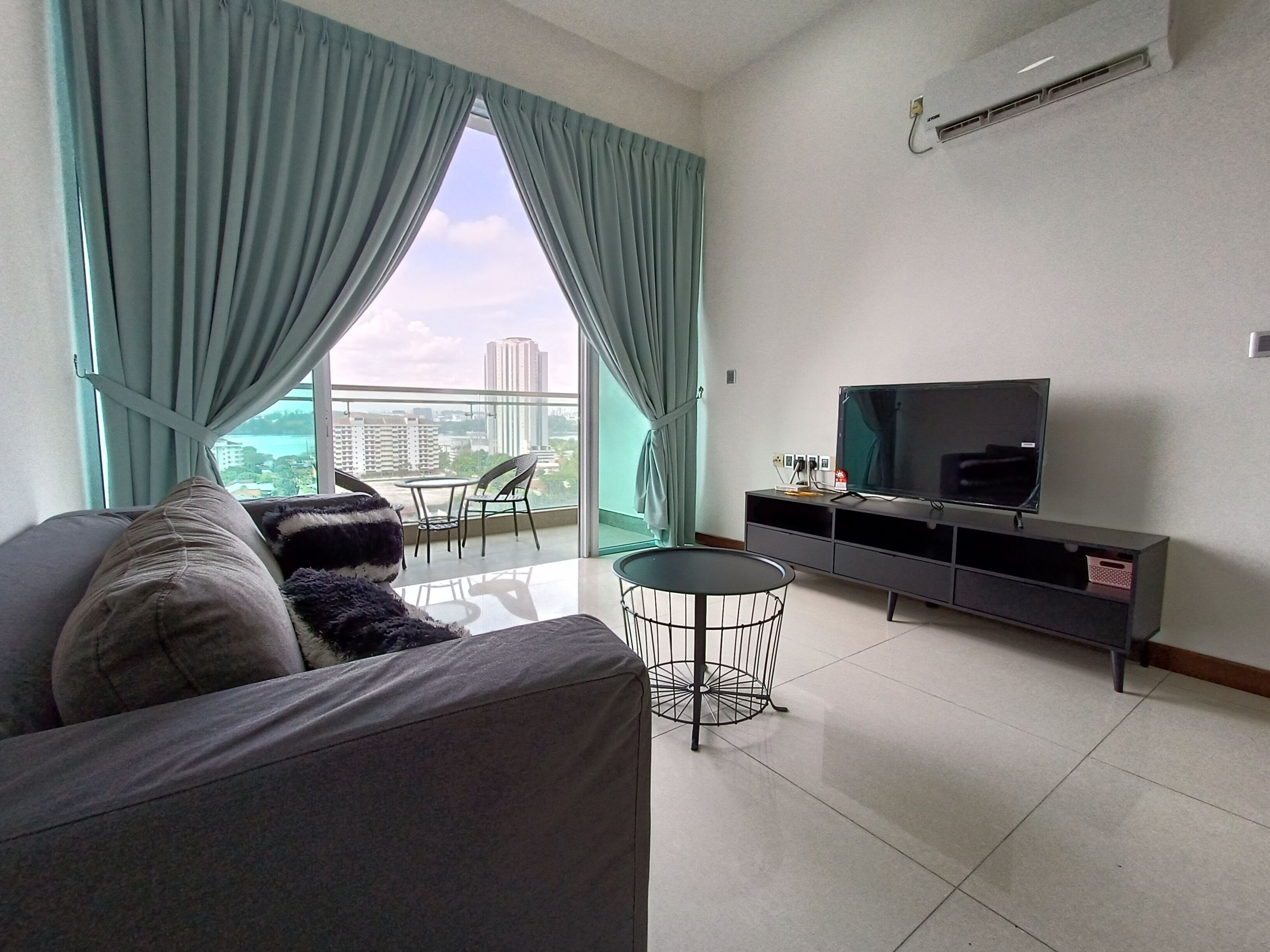 A modern living room with a grey sofa, a small round table, and a TV on a black stand.