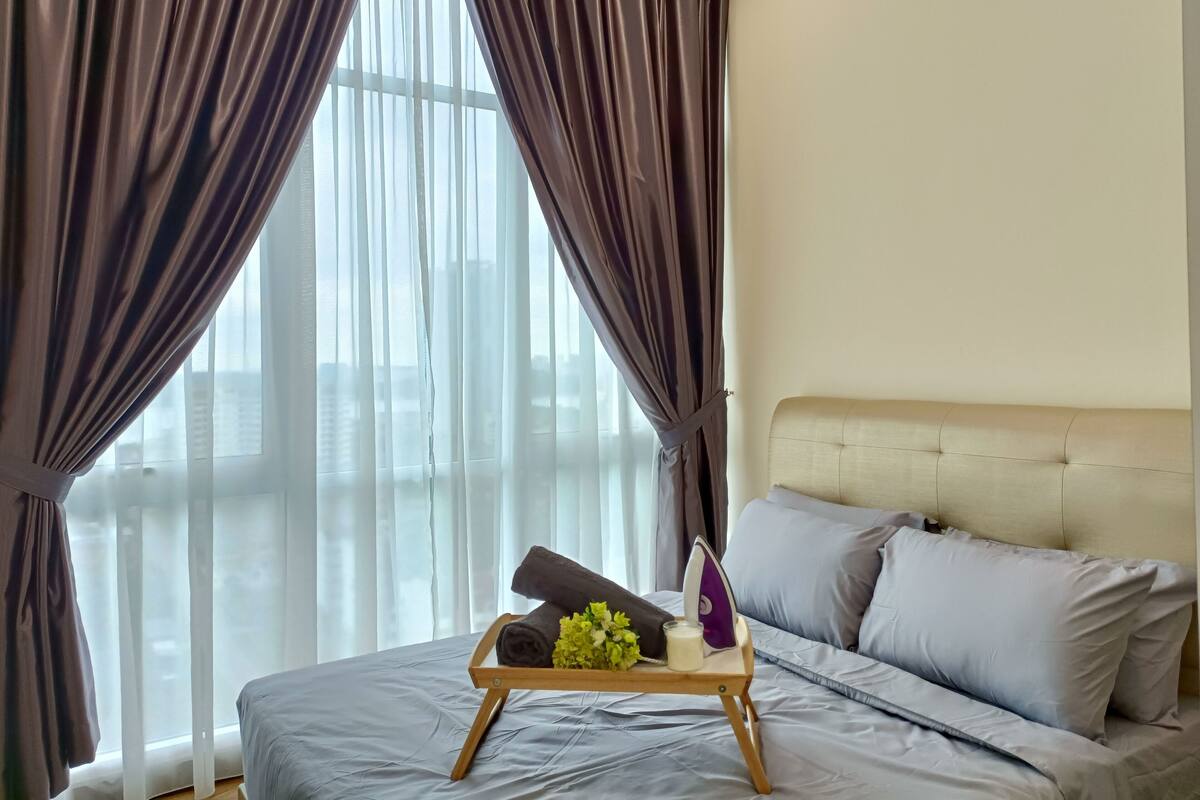 A hotel room with a bed, a bedside table with a tray of toiletries, and a window with curtains.