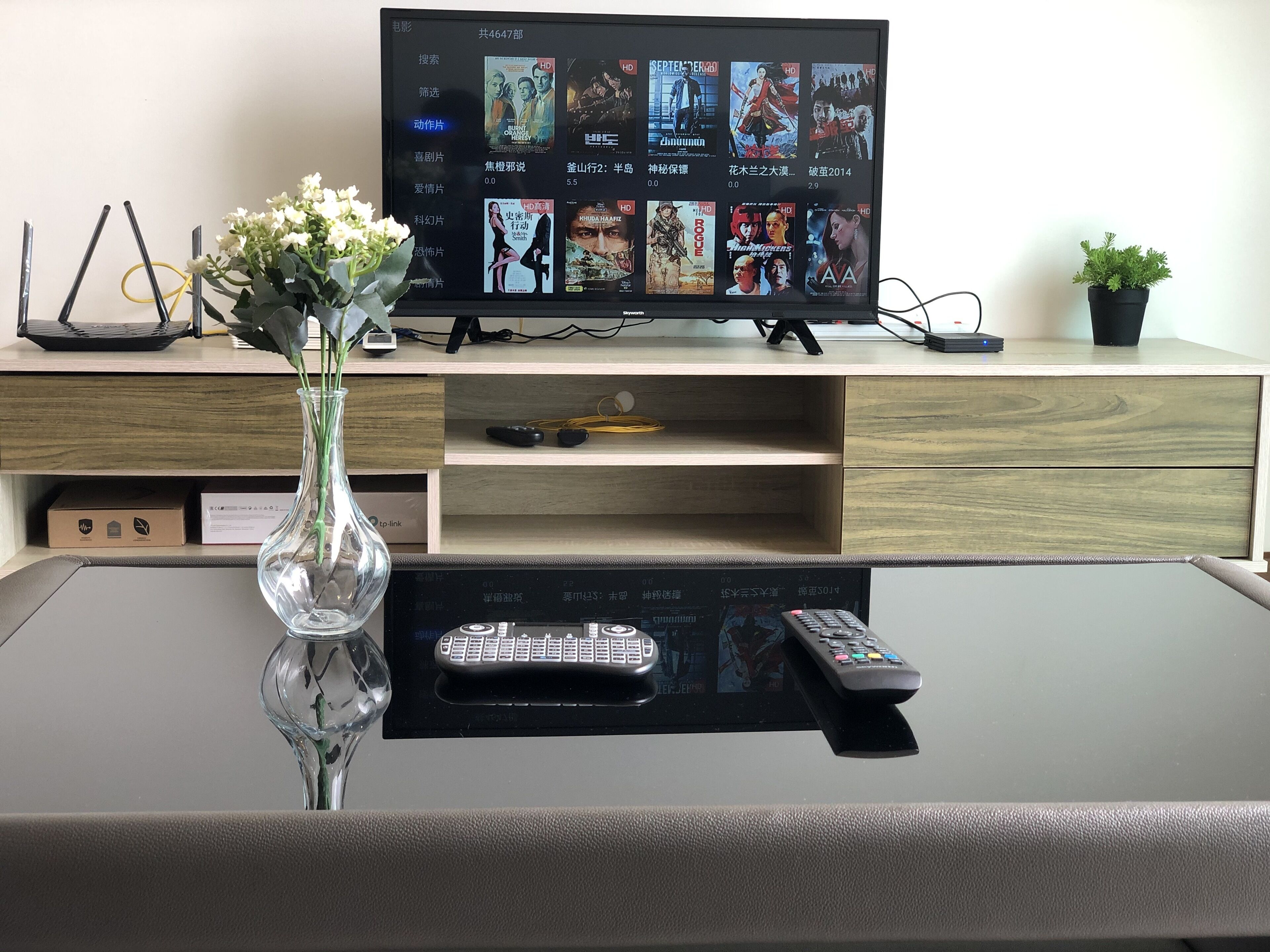 A TV on a wooden desk with a remote control and a vase with flowers.