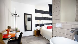 A modern hotel room with a bed, a desk, a chair, a large mirror, and a bathroom with a sink and toilet. - Lukanda Hospec Olehousing (Seville)