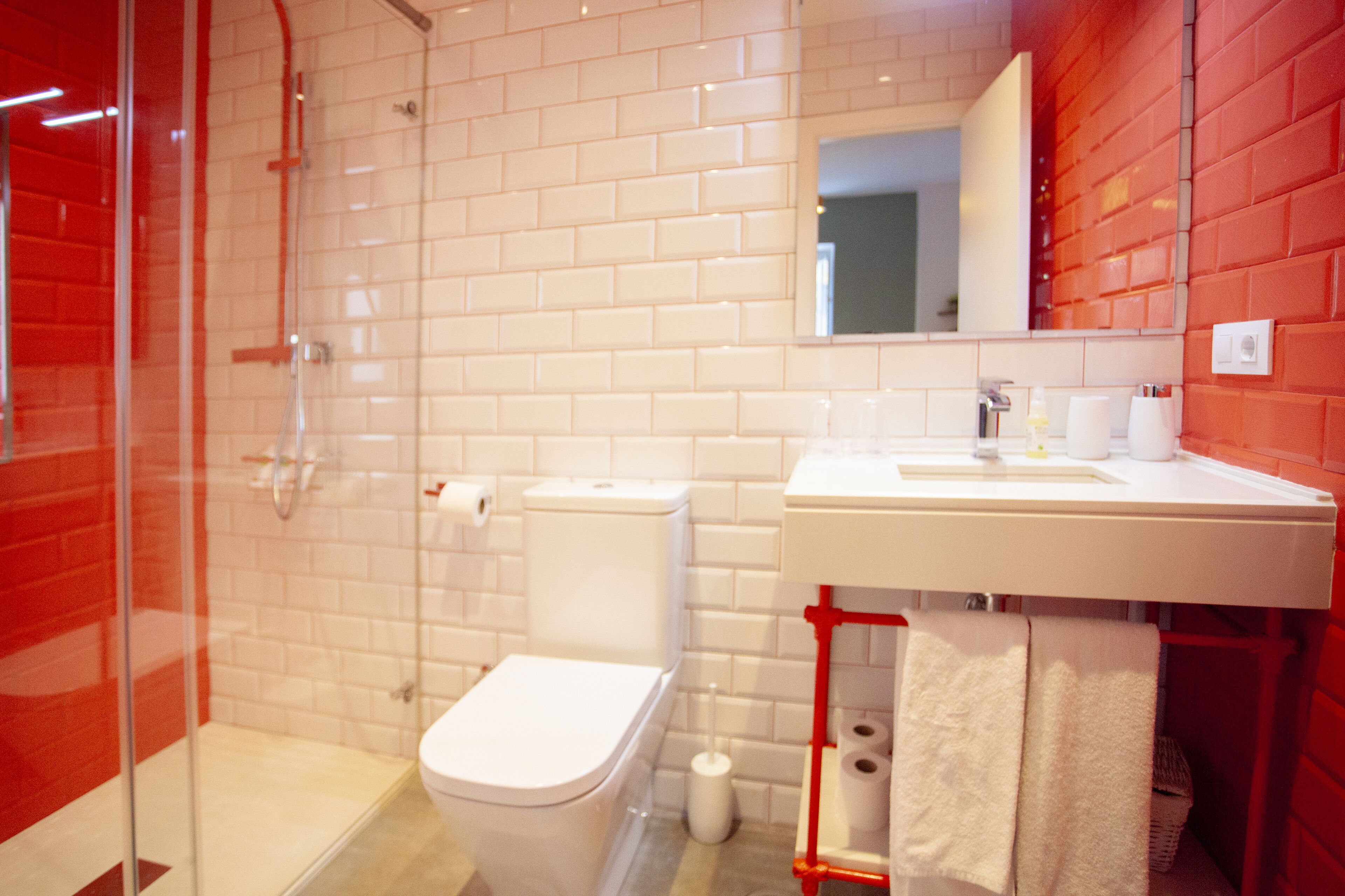 Un baño moderno con cabina de ducha de vidrio, un inodoro blanco y un revestimiento de pared de baldosas rojas.