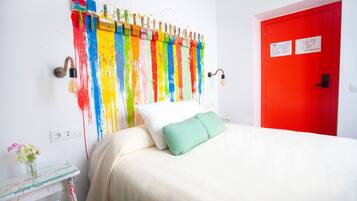 Une pièce avec un lit, une porte rouge et un mur orné d’éclaboussures de peinture colorées.