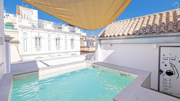 A rooftop swimming pool with a clear view of the cityscape, a shaded area, and a wall with a decorative mural. - Lukanda Hospec Olehousing (Seville)