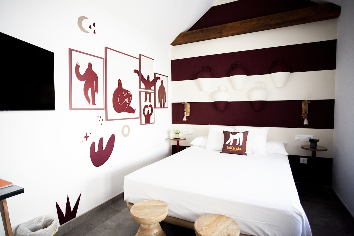 A hotel room with a large bed, a wall with decorative animal silhouettes, a wooden headboard, and two bedside tables.