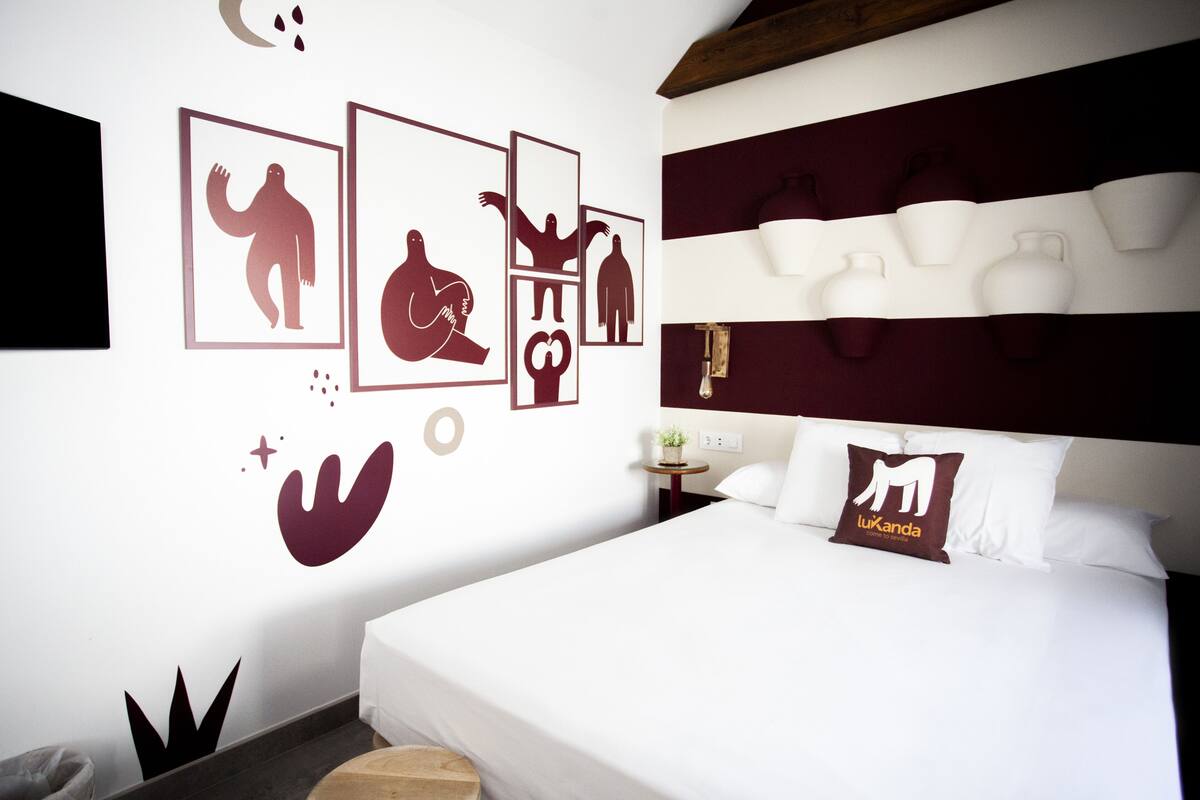 Moderni hotellihuone, jossa on suuri sänky, pääty, jossa on mukitelineet, ja seinillä abstrakteja kuvioita esittäviä taideteoksia.