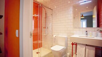 Een moderne badkamer met een douchecabine van glas, witte tegels, een wit wastafelmeubel en een rode handdoekhouder.