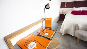 Habitación de hotel con cama, escritorio con material promocional, televisión y una pequeña mesa con una planta.