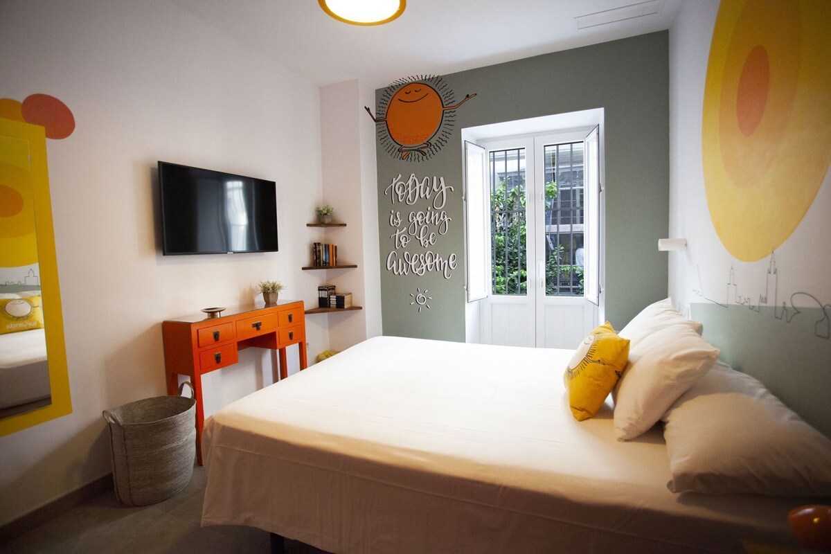A bedroom with a bed, a desk, a TV, a window, and a wall with a motivational quote.