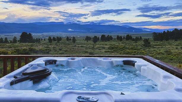 A hot tub with a view of mountains and a grassy landscape.