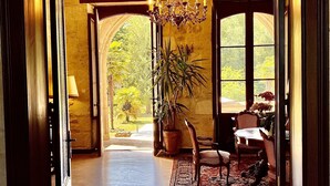 A spacious room with a high ceiling, a chandelier, a large window, and a dining area with a table and chairs. - Fairytale Chateau with pool surrounded by vineyard and parc (Blaye)