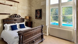 A bedroom with a large window, a wooden bed, and a radiator. - Fairytale Chateau with pool surrounded by vineyard and parc (Blaye)