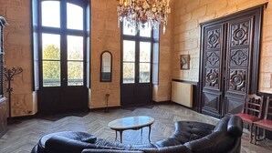 A cozy room with a large black leather sofa, a wooden ceiling, and a chandelier. - Fairytale Chateau with pool surrounded by vineyard and parc (Blaye)