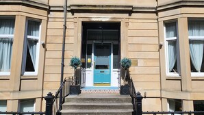 A building with a blue door, a staircase, and a small potted plant on the steps. - Boutique 50 (Glasgow)