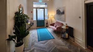 A hallway with a herringbone floor, a blue rug, a pink sofa, a chandelier, a painting, and a radiator. - Boutique 50 (Glasgow)