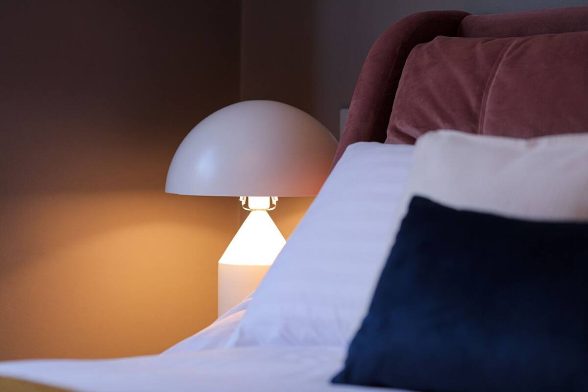 A bed with a white and navy pillow, a white lamp, and a red pillow.