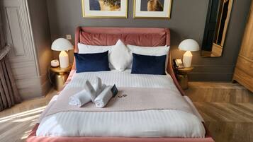 A neatly made bed with pink and white bedding, two framed pictures on the wall, and a bedside table with a lamp and phone.