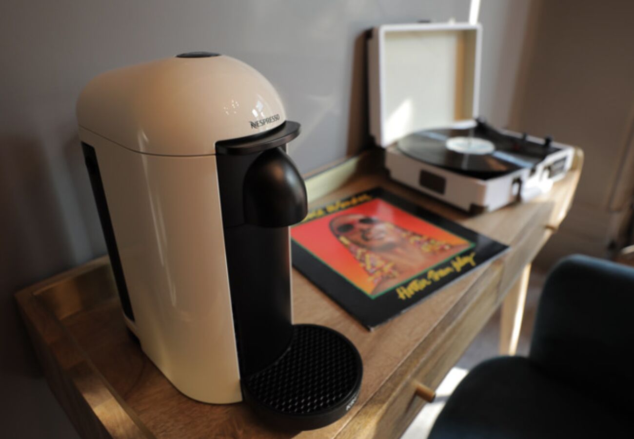 Una máquina de café Nespresso sobre una mesa de madera, junto a un tocadiscos de vinilo y un cuadro enmarcado.