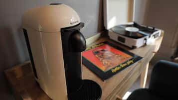 Una máquina de café Nespresso sobre una mesa de madera, junto a un tocadiscos de vinilo y un cuadro enmarcado.