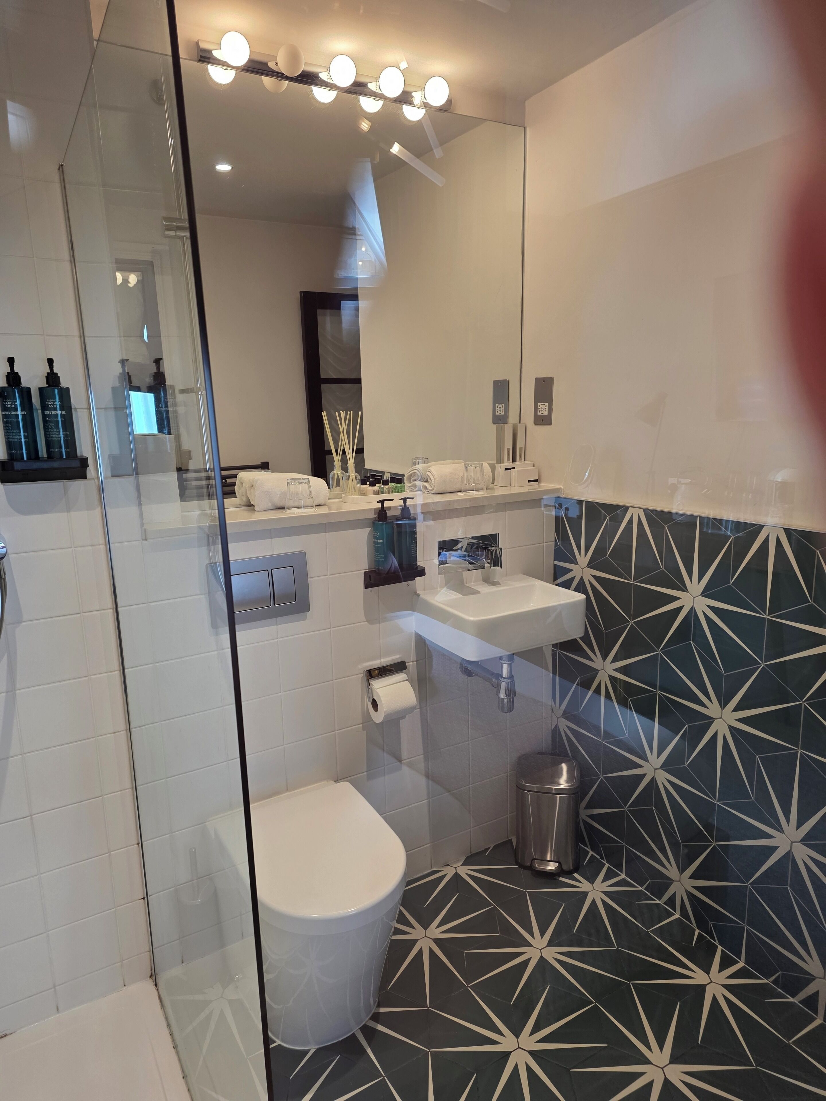 A modern bathroom with a glass shower enclosure, a white toilet, a sink with a mirror above it, and a patterned backsplash.