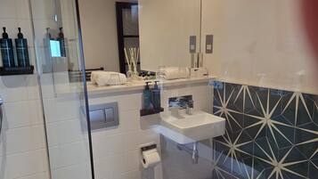A modern bathroom with a glass shower enclosure, a white toilet, a sink with a mirror above it, and a patterned backsplash.