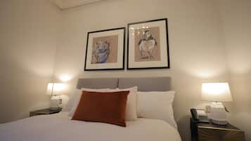 Una habitación de hotel con cama, dos ilustraciones enmarcadas de animales en la pared, una mesita de noche con lámpara y teléfono.