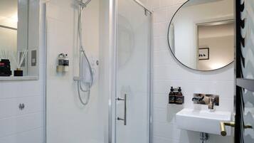 A modern bathroom with a glass-enclosed shower, white tiled walls, a white sink, and a geometric patterned floor.